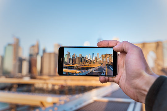 smartphone taking a picture of the skyline of new york from the brooklyn bridge