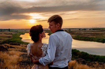 Loving couple, a guy and a girl kiss and hug at sunset on the mountain against the background of the river. Wedding day