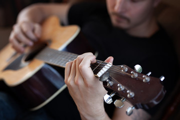 close-up portrait of a young man in black t-shirt playing an acoustic guitar. Focus is on his hand...