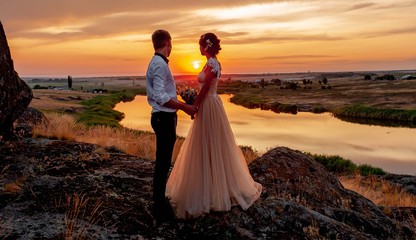 Loving couple, a guy and a girl kiss and hug at sunset on the mountain against the background of the river. Wedding day