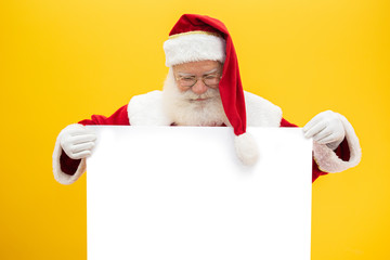 Fototapeta na wymiar Happy Santa Claus looking out from behind the blank sign isolated on yellow background with copy space