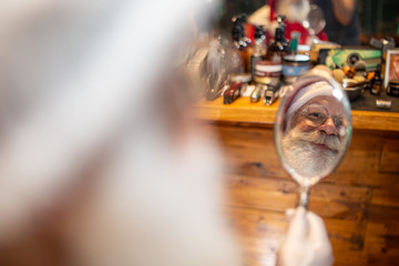Santa Claus shaving in barbershop. Looking in the mirror. Getting ready for Christmas. Beautifying for the holidays. Bearded. Cuting.