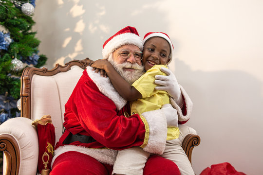 Santa Claus delivering a gift box to a little African boy. Hug. Christmas eve, delivery of gifts.