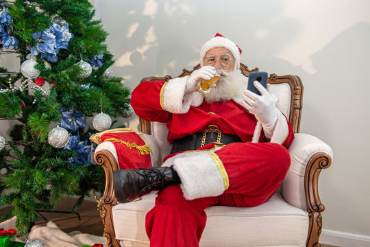 Santa Claus drinking a glass of beer while using his cellphone. Rest time. Alcoholic drink at the holidays. Drink with moderation. Craft beer. Merry Christmas.