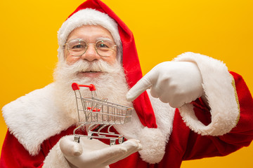 Santa Claus and the supermarket, he is showing a mini cart. Christmas and shopping concept.