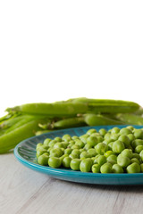 Garden peas with pods on a blue plate.  Grey wood background
