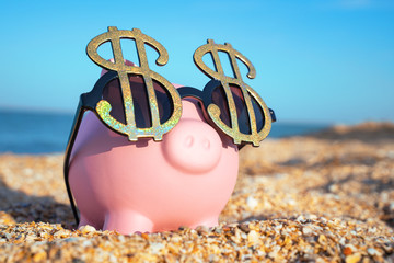 Holiday savings pink piggy bank on a beach vacation with dollar sign sunglasses