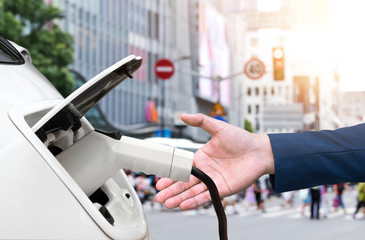 EV automotive , Air pollution and reduce greenhouse gas emissions concept. Hand holding and charging Electric car with blur city view background.