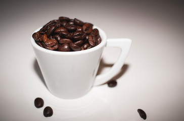 Kaffeebohnen in Espressotasse mit Henkel gefüllt vor weissem Hintergrund