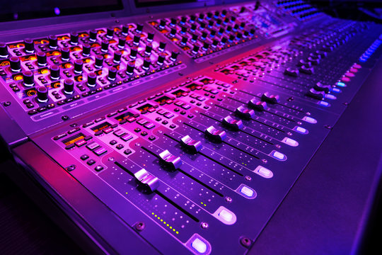 Professional audio studio sound mixer console board panel with recording , faders and adjusting knobs,TV equipment. Blue and red tone and close-up image with flare light effect.