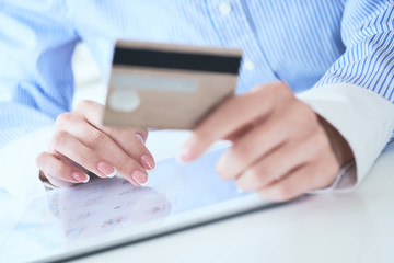 Close-up woman's hands holding a credit card and using tablet pc for online shopping. Middle section of young businesswoman making online payments with credit card and tablet.