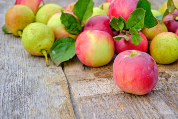 Fresh seasonal red apples and pears with green leaves on an old wooden table.