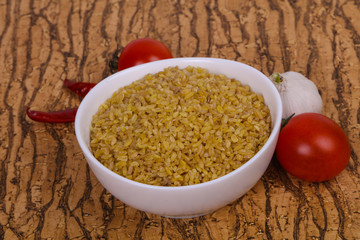 Raw bulgur in the bowl with tomatoes and garlic