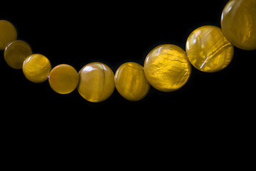 Yellow necklace made of round flat beads on a dark background close up