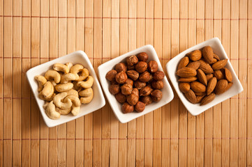 three white bowls filled with nuts - hazelnuts, almonds and cashews