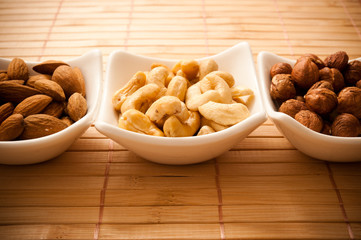 three white bowls filled with nuts - hazelnuts, almonds and cashews