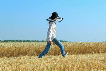 Carefree and attractive young woman in a wheat field. People, nature, farming concept. Young girl walking outdoors.