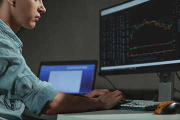 Cropped shot of a young man using two computers for stock trading. Unrecognizable program developer working late in the evening