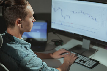 Rear view shot of a young male businessman working after hours in a dark office. Program developer working online late at night