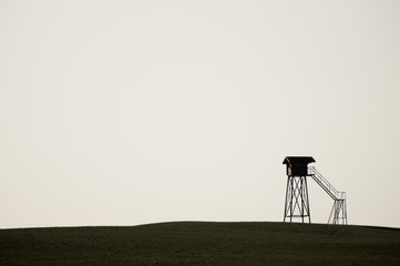 Naklejka premium Lonely watch tower. observation post standing alone on the hill. hunting lodge in the field. solitude concept