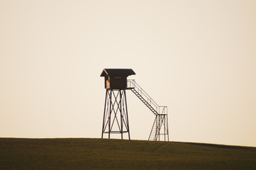 Naklejka premium Lonely watch tower. observation post standing alone on the hill. hunting lodge in the field. solitude concept
