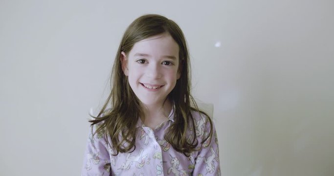 Young girl says I love you with hand gestures by pointing to her eye, then makes a heart with her hands then points at the camera while smiling and laughing