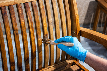 Adult carpenter craftsman painting with water-based paint the strips of a chair wooden garden. Housework, do it yourself. 