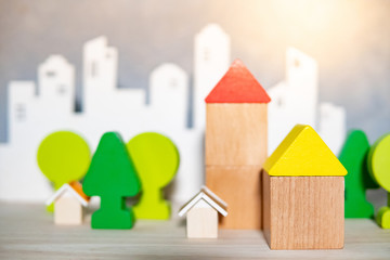 Group of wooden house and tree toy models with blurred city background on the table. Urban living concept