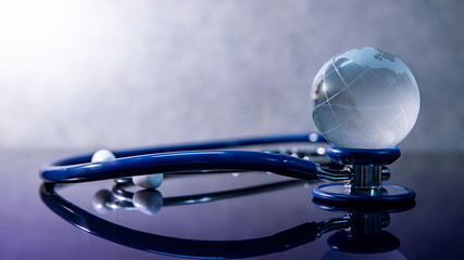 Global healthcare concept. World globe crystal glass on blue stethoscope on glossy desk. Health and medical science. Worldwide wellness business