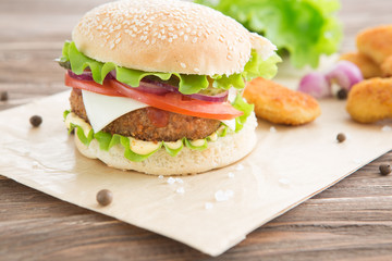 Delicious fast food. Cheese burger with grilled meat, cheese, tomato, on craft paper on wooden surface. Fast food template. Real photo. ideal for advertisement