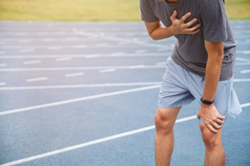 Man runner athlete chest injury and pain. Man suffering from painful chest or Symptoms of heart disease while running on the blue rubberized running track.