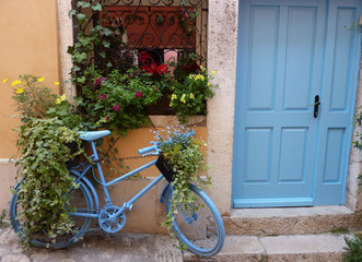 Fototapeta na wymiar Blaues Fahrrad vor gelber Hauswand und blauer Haustür mit Blumen