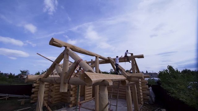 Builders working on construction of wooden cottage. Clip. Construction of wooden house of logs with working workers on background of blue sky