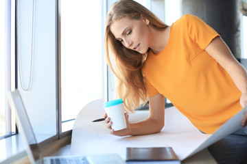 Beautiful modern woman is writing something down on the blueprint while working in the creative office