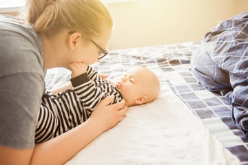 Caucasian Tender mother and baby are lying on the bed,, gently touches the baby, The concept of motherhood, trust and protection. Lifestyle and light toning