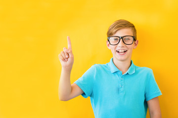 Portrait of stylish little boy with finger pointed up. Kid on yellow blackboard. Success, bright idea, creative ideas and innovation technology concept