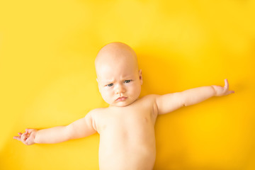 Cute baby lies arms outstretched on a yellow background