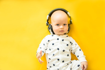 Baby with headphone lies on yellow background