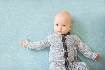 Calm curious baby lying on blue background, looking at camera, top view
