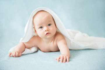 Happy baby with a towel after the shower in bed at home