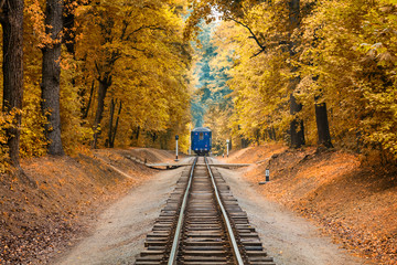 Beautiful autumn forest and old colorful blue railway train locomotive on the track rails.