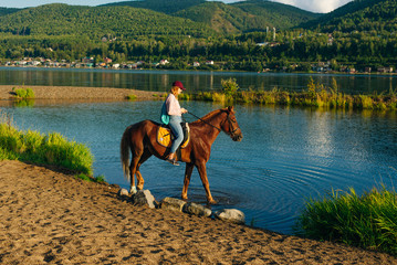 girl on a brown horse by the pond