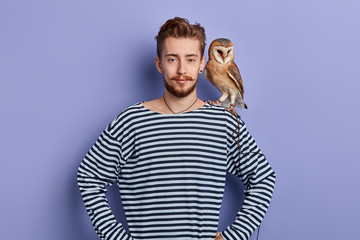 young man going to show tricks with an owl, isolated blue background, studio shot. clown having...