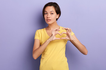 beautiful young american womanmaking heart gesture, close up portrait, isolated blue background, studio shot, body language, isolated blue background.love, feeling and emotion