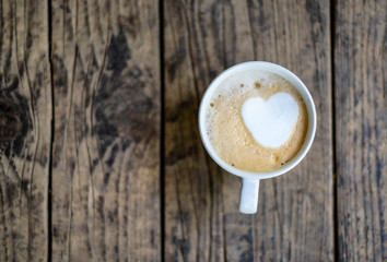 A cup of coffee with a heart in a white cup on the wooden background