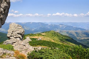 Landscape of high mountains with huge stones on top of the hillside and hills with cloudy sky. Carpathian mountains in summer