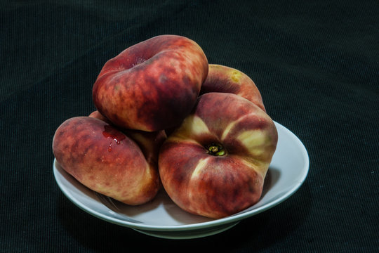 Flat peaches (Prunus persica var. platycarpa) in a deep plate on the dark background