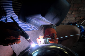 man works argon welding repairs aluminum pipe in the garage of the house