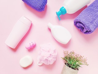 Obraz na płótnie Canvas Flat lay photo toiletries set. Natural organic cosmetics. Herbal shampoo, shower gel, liquid soap, purple towel, sponge, rubber toy hippo and flowers on a pink background