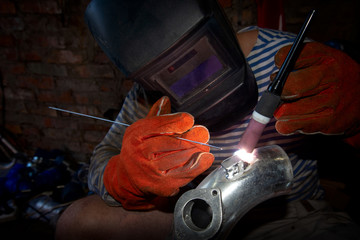 man works argon welding repairs aluminum pipe in the garage of the house